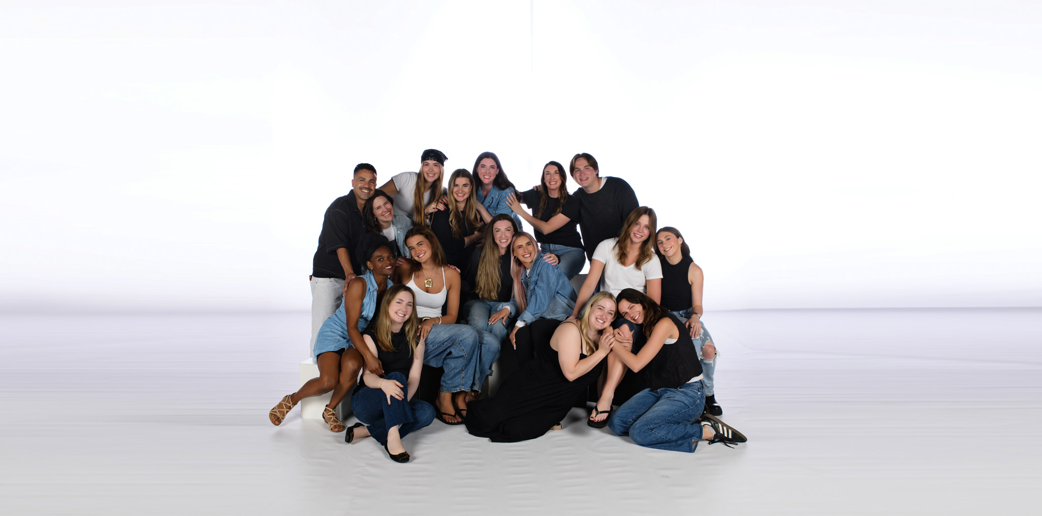 Group of about 15 diverse friends posing together in a bright studio, smiling and embracing.