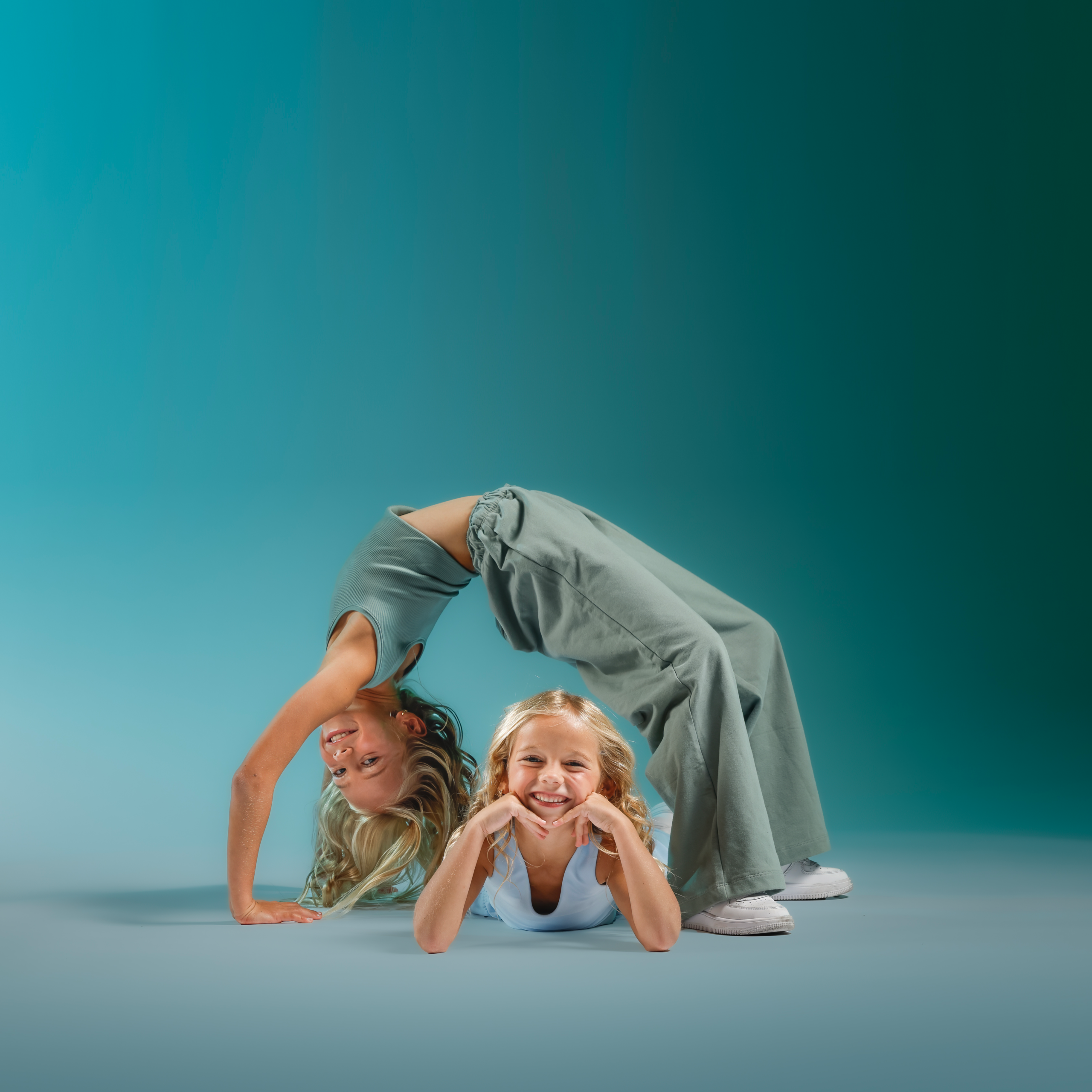 Four children crouch and bend with their heads together, smiling at the camera on a blue-tinted background.