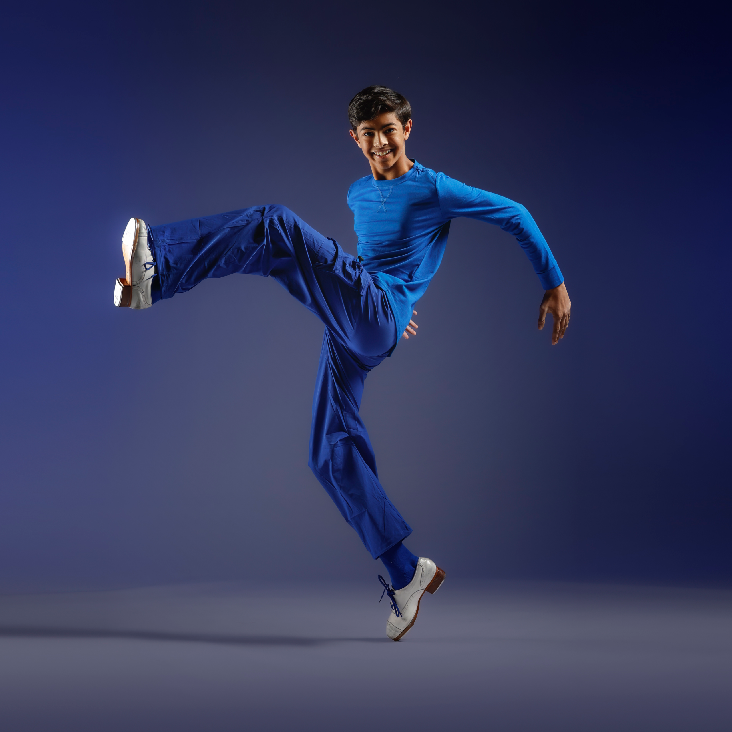 Young man in a blue athletic outfit jumping midair against a dark blue gradient background